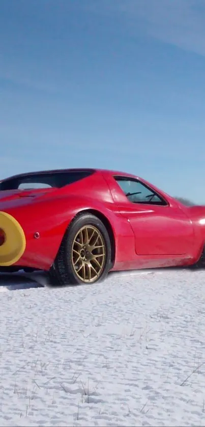 Red sports car on snowy field under blue sky.