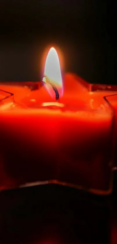 Star-shaped red candle with a glowing flame in a dark setting.