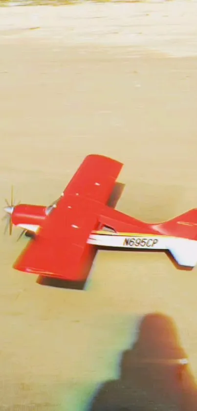 Red toy airplane model on sandy ground.