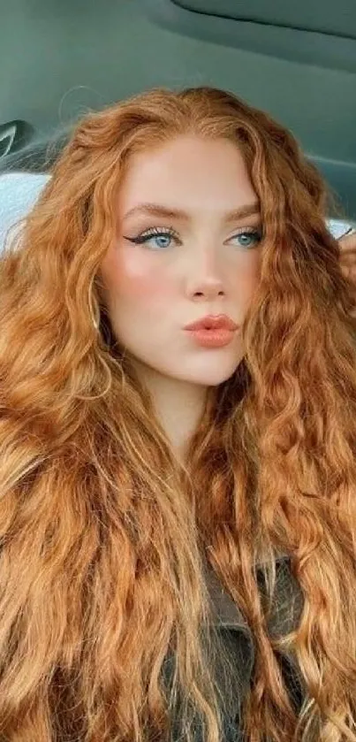 Red-haired woman poses in car with vibrant, natural curls.