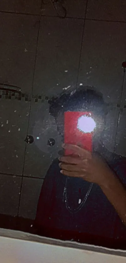 Reflective selfie in a dark mirror with red phone flash.