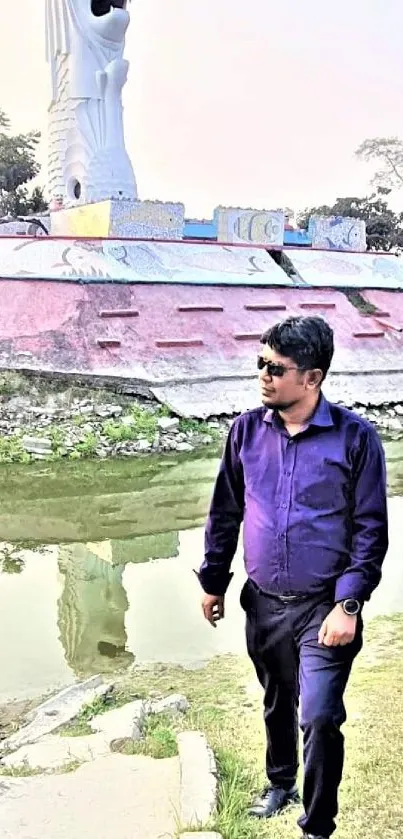 Man in purple shirt walks near a statue and pond reflecting scenery.