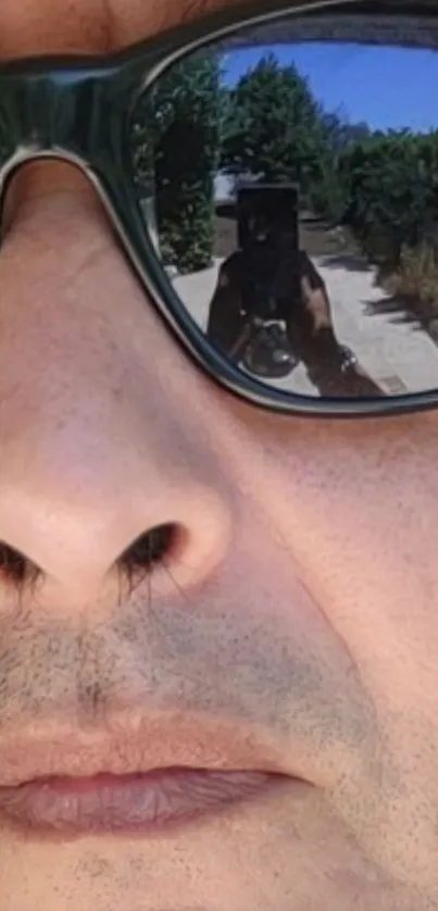 Close-up of face with reflective sunglasses showing outdoor scene.