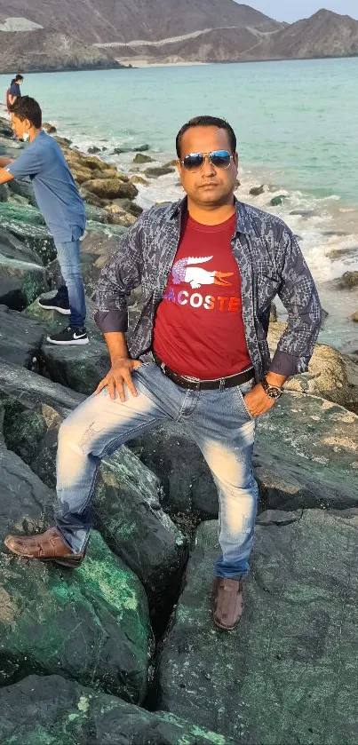 Man posing on rocky beach shore in front of turquoise ocean.