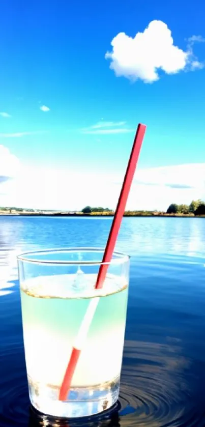 Glass with drink by a serene blue lake under a bright sky.