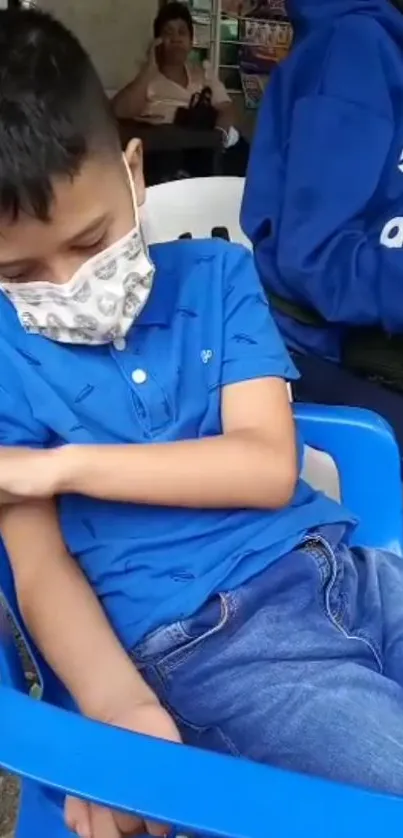 Boy relaxing in blue chair, wearing a face mask, capturing calm and safety.