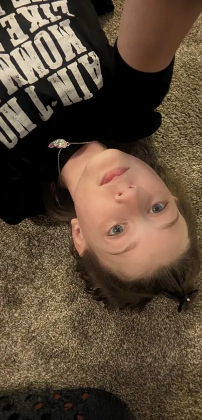 A child lying on a brown carpet wearing a black graphic tee.