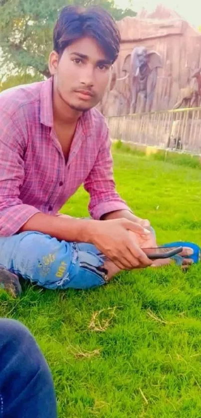 Young man in casual attire sitting on a green lawn.