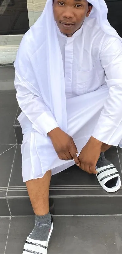 Young man in modern white attire sitting on steps.