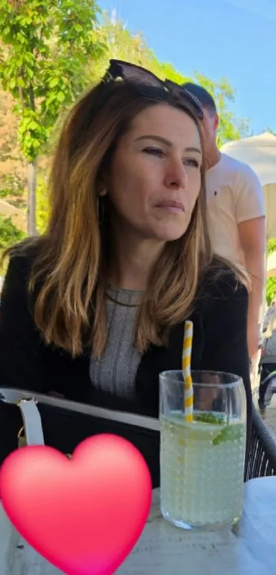 Woman enjoying a sunny day at an outdoor cafe with a lemon drink.