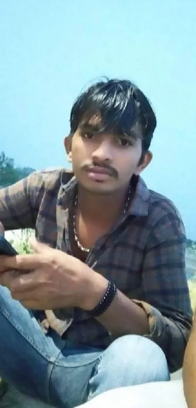 Young man outdoors with smartphone and serene sky.