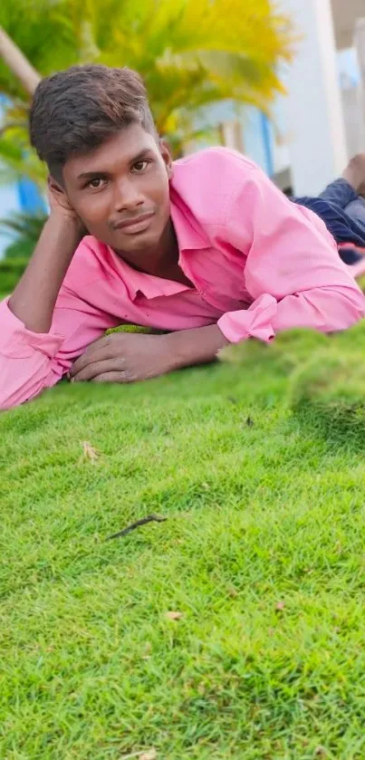 Young man in pink shirt relaxing on green grass outdoors.