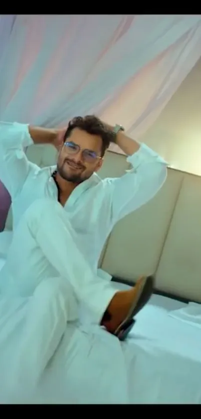 Man lounging on bed in white-themed bedroom.