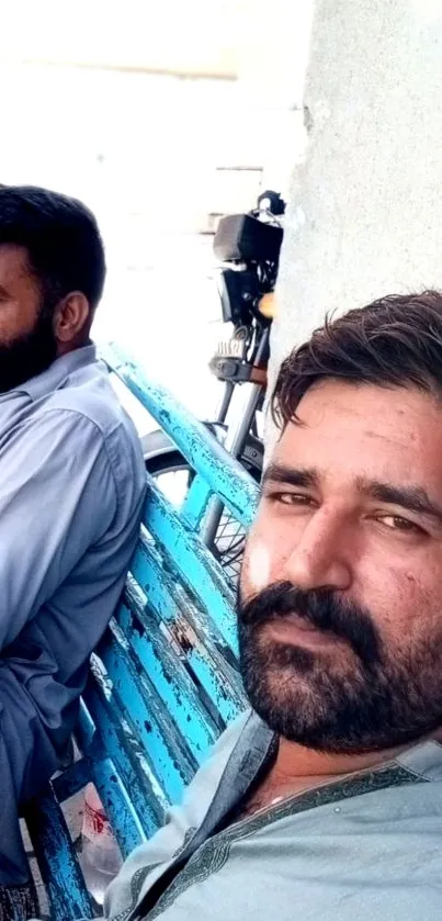 Two men sitting on a bright blue bench, enjoying a relaxed moment.