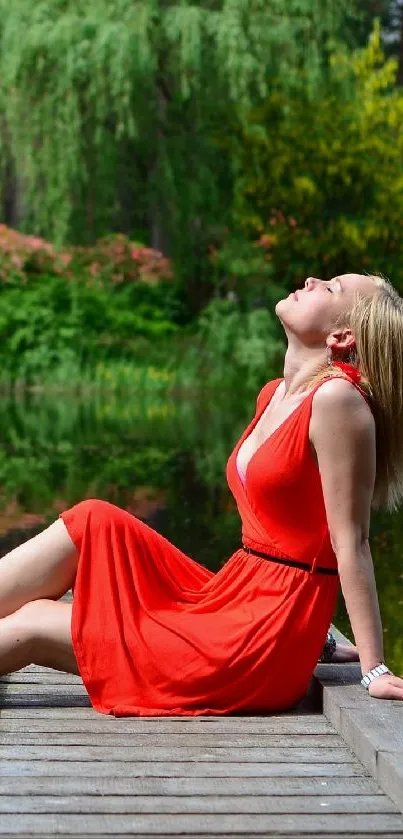 Woman in a red dress relaxing by a lake with lush greenery.