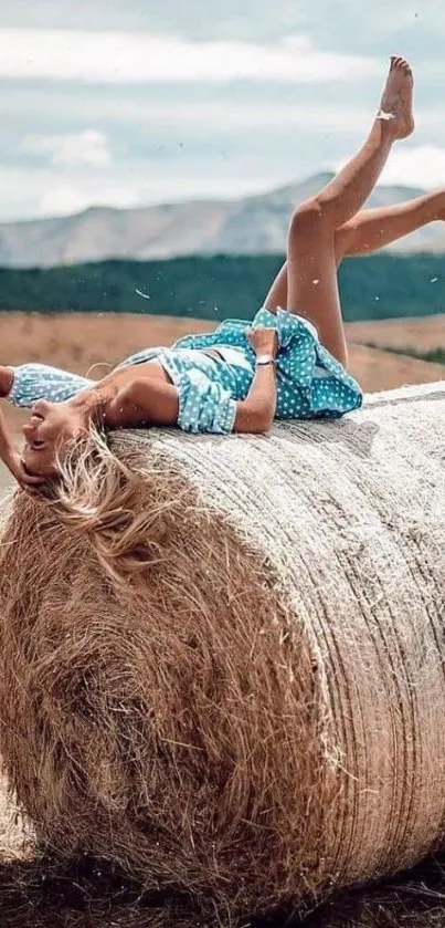 Woman in blue dress relaxing on hay bale in open field.