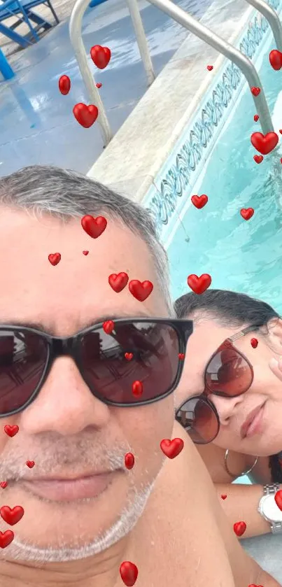 Couple taking a selfie by the pool, wearing sunglasses.