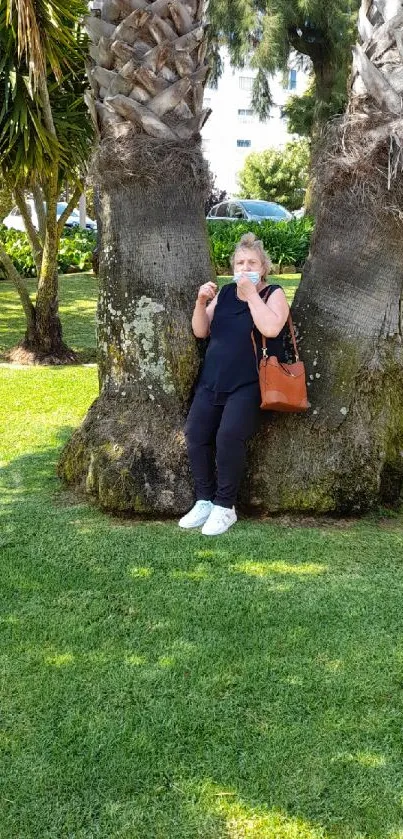 Woman relaxing under palm trees in a park with green grass.