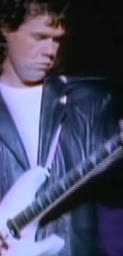 Guitarist in black leather jacket playing a white electric guitar on stage.