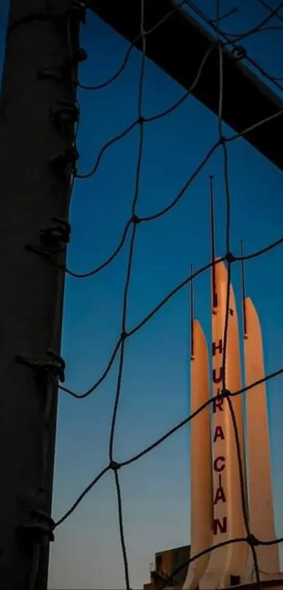 Silhouette of a rocket against a sunset sky through netting.