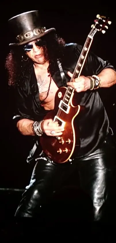 Guitarist playing on stage in stylish black outfit with leather pants.