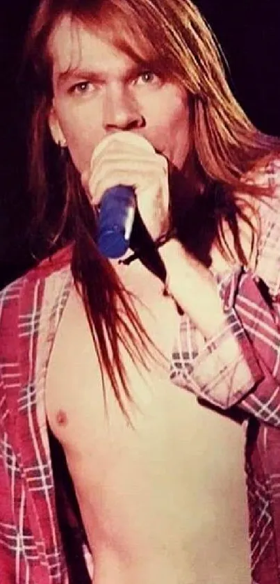 Rockstar in a plaid shirt performing live on stage, holding a microphone.