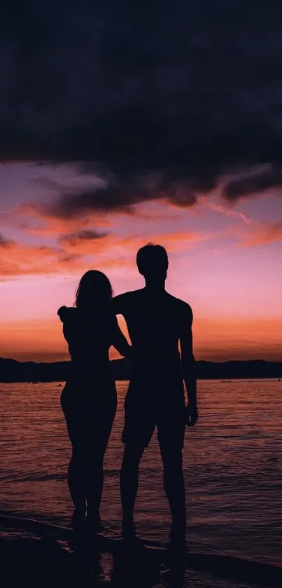 Silhouette of couple at beach sunset with purple hues.