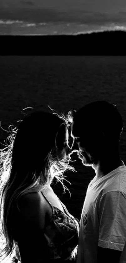 Romantic couple silhouette by water in black and white photo.