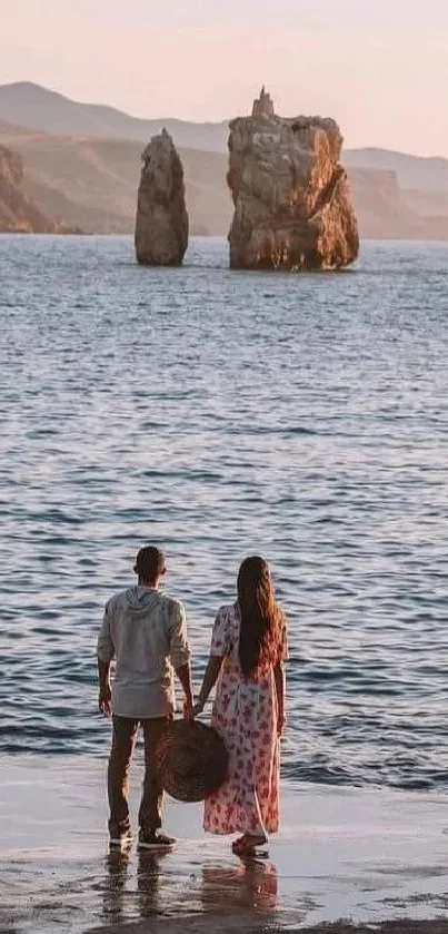 Couple gazing at sunset over the sea with rock formations.