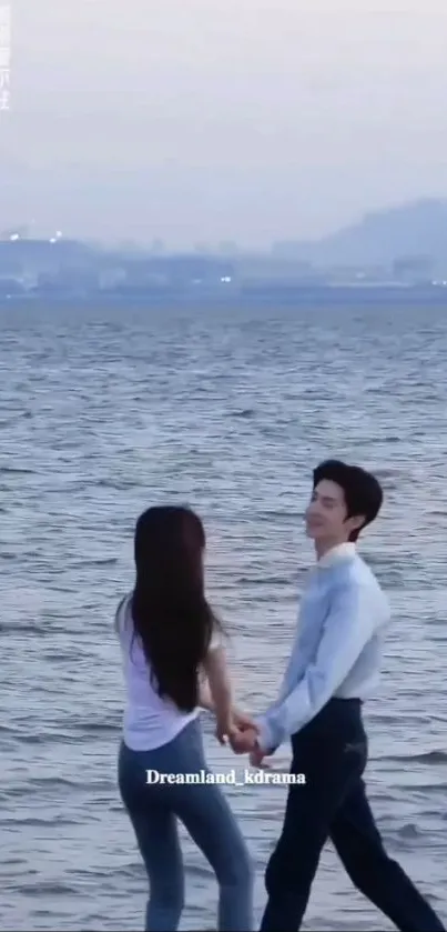 A couple holding hands by the sea with city in the background.