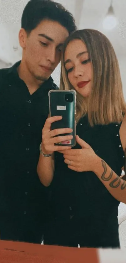 Romantic couple taking a mirror selfie, dressed in dark outfits.