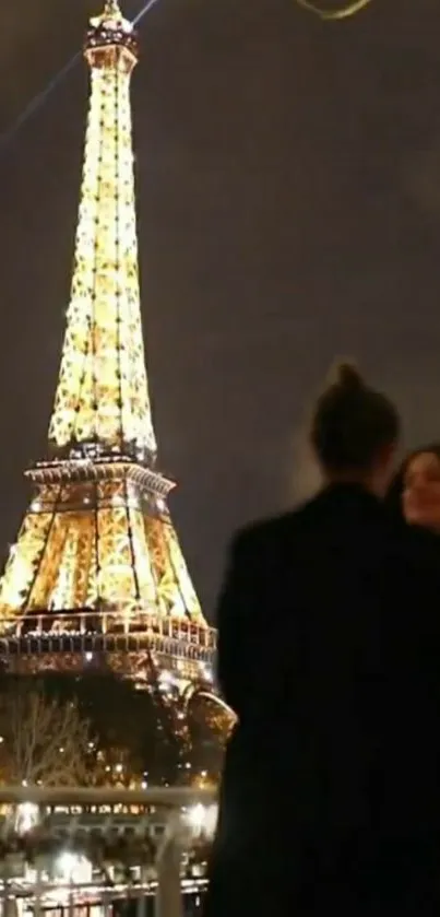 Silhouette of couple with Eiffel Tower glowing at night.