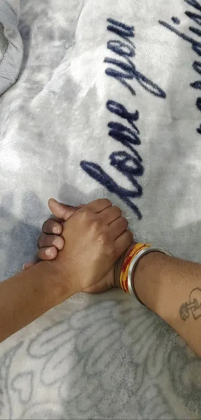 Couple holding hands on a light gray blanket.