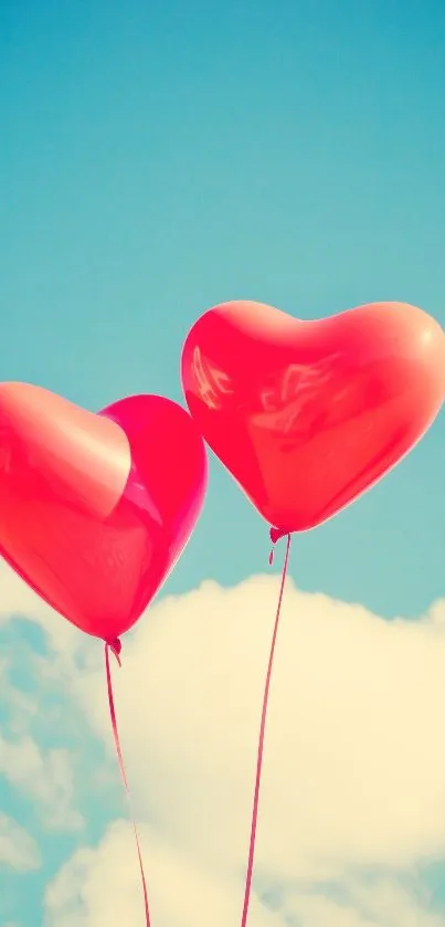 Two red heart-shaped balloons float against a clear blue sky.