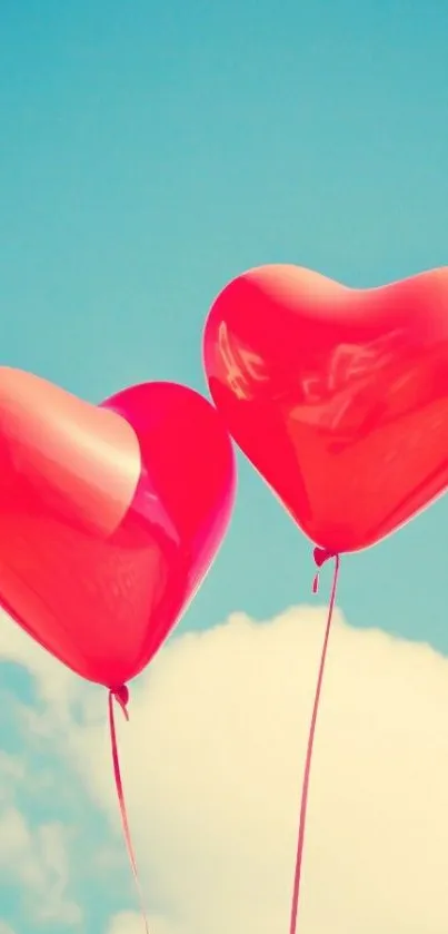 Two red heart balloons floating in a blue sky with clouds.