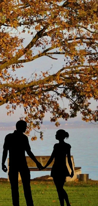 Romantic silhouette of a couple under an autumn tree by the lake.