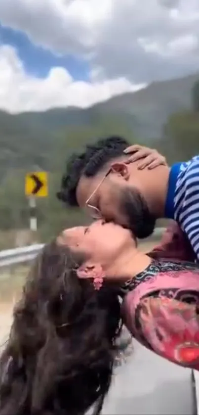 Couple kissing on mountain road with scenic backdrop.