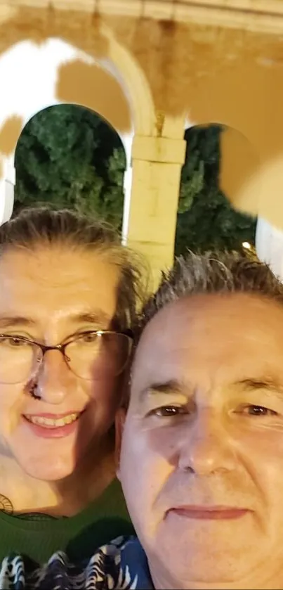 Couple smiling in front of ancient illuminated arches.