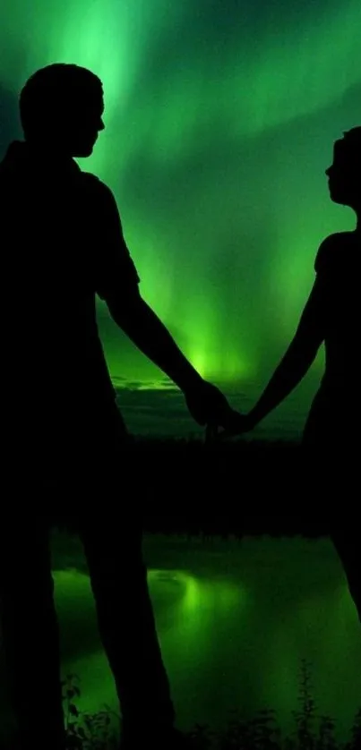 Silhouette of a couple holding hands against the Northern Lights on a night sky backdrop.