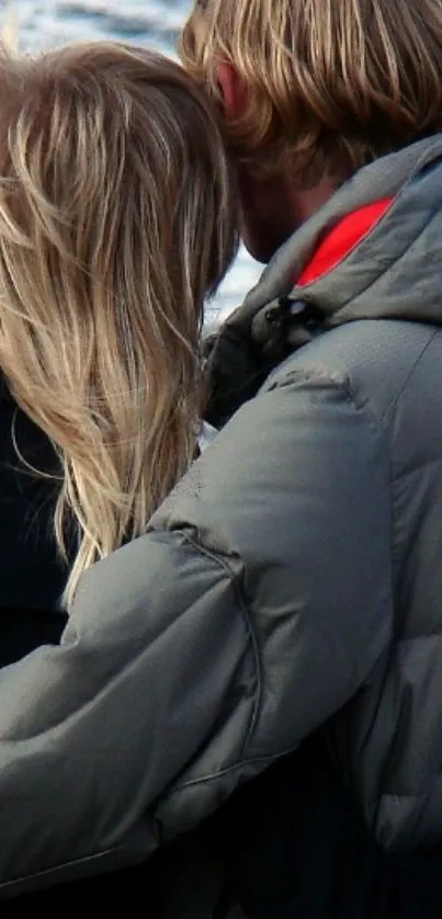 Romantic couple embracing by the ocean in cozy winter jackets.