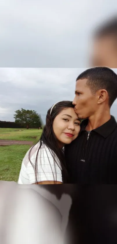 A couple embracing outdoors, surrounded by green and sky.