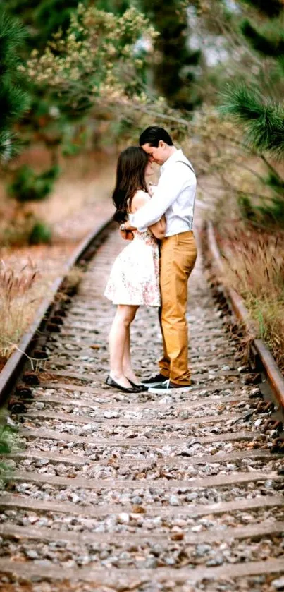 Couple embracing on vintage railway tracks in a lush green setting.