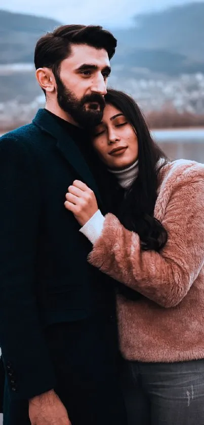 Couple embracing by the lake with mountain backdrop.