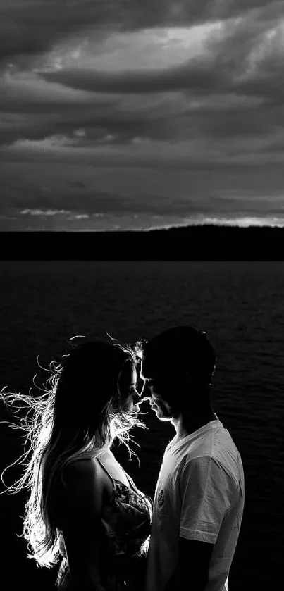 Silhouette of a couple by the lake under a cloudy sky in black and white.