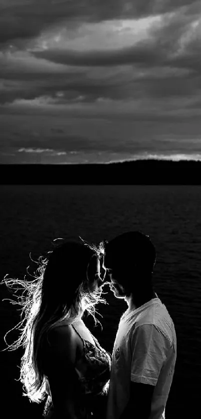 Black and white wallpaper of a couple silhouetted by a lake under a dramatic sky.
