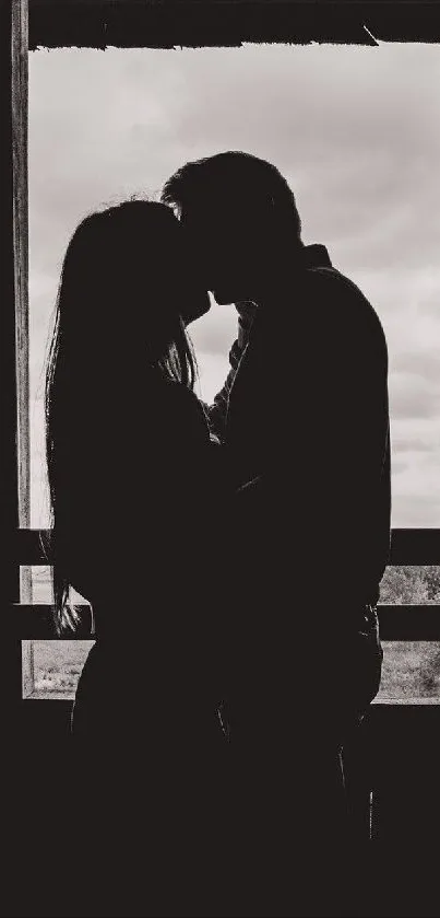 Silhouette of a couple kissing in front of a window.