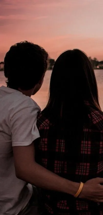 Couple sitting by lake at sunset, embracing under a pink sky.