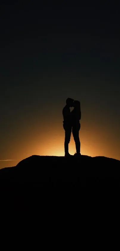 Couple silhouette against a sunset background on a hill.