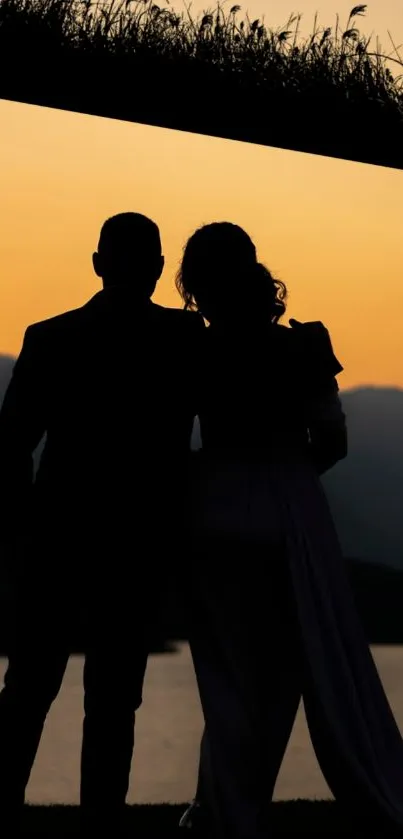 Silhouetted couple against a sunset over water and mountains.