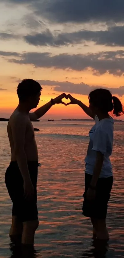 Silhouette of a couple making a heart shape at sunset on the beach.